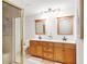 Bright bathroom boasts a double vanity with wooden cabinets, framed mirrors, and a tiled shower with a gold frame at 4718 Valley Hill Ct, Lakeland, FL 33813