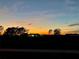 Beautiful single-story home in distant shot with a colorful sunset sky backdrop at 705 Lake Ada Blvd, Dundee, FL 33838