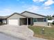 Single-story home features a two car garage, stone paver driveway, manicured lawn, and neutral-colored exterior at 1957 Prairie Dunes N Cir, Lakeland, FL 33810