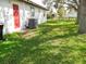 Lush backyard featuring a red door and a modern air conditioning unit, with a mature shade tree at 2111 Groveglen S Ln, Lakeland, FL 33813