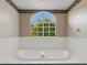 Bright white bathroom with a large soaking tub under a window with a view of mature landscaping at 324 Lake Mariam Blvd, Winter Haven, FL 33884