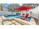 Inviting pool area with a red umbrella, chairs, and decorative elements against a white fence at 511 Mcrorie St, Lakeland, FL 33803