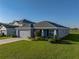 View of a single-story home with a gray exterior, well-manicured lawn and landscaping, and a two-car garage at 236 Talladega Ln, Polk City, FL 33868