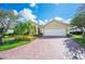 Charming tan single-story home featuring mature landscaping, a brick paver driveway, and a two-car garage at 2900 Grasslands Dr, Lakeland, FL 33803