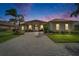 Elegant home featuring stucco facade, arched windows, double door entry, manicured landscaping, and brick paver driveway at dusk at 565 Osprey Landing Dr, Lakeland, FL 33813