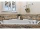Elegant soaking tub with granite surround and modern fixtures under a window with plantation shutters at 7010 Parliament Pl, Lakeland, FL 33809