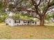 Charming single-story white home featuring dark shutters and a welcoming porch swing, shaded by a large mature tree at 135 Kenilwood Ln, Lakeland, FL 33809
