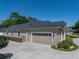 Attached three-car garage with a tan door and a gray roof, framed by manicured shrubs and green lawn at 152 Melissa Trl, Auburndale, FL 33823