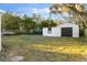 View of the detached garage with black door situated on a large lot surrounded by trees and greenery at 126 Mason St, Auburndale, FL 33823
