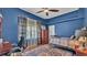 A blue bedroom includes a desk, a bed with plaid blankets, windows, and a view of the backyard at 5638 Bloomfield Blvd, Lakeland, FL 33810