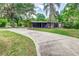 Wide concrete driveway leading to a single-story home with a carport, green lawn, and mature trees, offering ample parking at 1604 Sylvester Rd, Lakeland, FL 33803