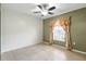 Neutral bedroom boasts ceiling fan, tile floors, and window with ornamental drapes at 7139 Cedarcrest Blvd, Lakeland, FL 33810