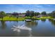 Aerial view of a serene lake featuring a fountain, lush greenery, a dock, and community amenities under a clear sky at 4965 Goldenview Ln, Lakeland, FL 33811