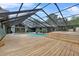 A screened in pool with a large wooden deck, jacuzzi, and green home in the background at 3805 Gaines Dr, Winter Haven, FL 33884