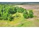 Aerial view of a lush, vibrant green forest bordering a large grassy field with a rustic fence line at 14810 Brahma Rd, Polk City, FL 33868
