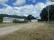 Wide view showcasing a mobile home, shed, and canopy in a rural setting with a long gravel driveway at 14810 Brahma Rd, Polk City, FL 33868