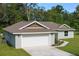 Single-story home with a two-car garage and driveway, surrounded by a spacious grassy lawn and mature trees at 10470 Sw 139Th Ct, Dunnellon, FL 34432