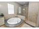 A bright bathroom features a tub, walk-in shower with glass surround, travertine tile, and vanity at 843 Christina Chase Dr, Lakeland, FL 33813