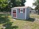 New gray storage shed with red and white trim, window, and door on a grassy lot with chain-link fence at 355 E Columbia St, Lake Alfred, FL 33850