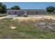 View of the back of this single-story home with gray siding and a dark roof with a yard full of grass and dirt at 246 Quail Run, Frostproof, FL 33843