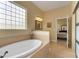 Bathroom featuring a tiled soaking tub, glass block window, and a view into the adjacent bedroom at 2731 Coventry Ave, Lakeland, FL 33803
