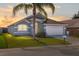Charming single-story home with a well-manicured lawn and mature palm tree set against a colorful sunset sky at 436 Lady Diana Dr, Davenport, FL 33837