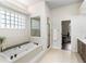Bright bathroom with tiled flooring, soaking tub with jets, glass block window and shower, and a dark vanity at 4642 Highlands Place Dr, Lakeland, FL 33813