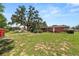 A large backyard featuring mature trees, partial grass, and a charming red storage shed at 111 E Orange St, Davenport, FL 33837