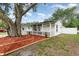 Charming one-story home with a covered porch, picket fence, and fresh landscaping featuring a large mature tree at 113 Patrick Henry Rd, Bartow, FL 33830