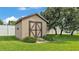 View of backyard shed with green lawn, bordered by a white fence and mature landscaping at 118 Caloosa Dr, Babson Park, FL 33827