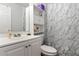 Well-lit bathroom featuring a vanity, toilet, and shower with stylish marble-patterned walls at 3016 Reiter Dr, Auburndale, FL 33823