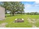 Backyard featuring a stone fire pit, grass, trees, and a house in the distance at 2911 Walker Rd, Lakeland, FL 33810