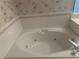 Relaxing jetted bathtub with white tile surround and decorative wallpaper for a spa-like experience at 5480 Summerland Hills Dr, Lakeland, FL 33812