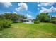 Expansive backyard featuring lush green grass, mature trees, a pool, and a screened lanai under a sunny sky at 5619 Stratford Ln, Lakeland, FL 33813