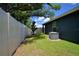 White fence encloses the neutral colored home with green grass and trees, and an air conditioner at 312 Walnut Ln, Auburndale, FL 33823
