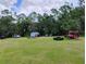Open backyard with lush grass and a backdrop of mature trees, accented by parked cars and storage sheds at 6915 Dove Meadow Trl, Lakeland, FL 33810
