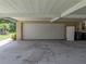 View of the open carport with a white garage door and access to a residential trash receptacle at 1232 Fairlee St, Lakeland, FL 33813