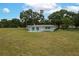 Single story home featuring a spacious lawn, mature trees, and a patio with colorful chairs on a sunny day at 21 Lake Ave, Winter Haven, FL 33880