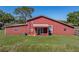 Rear view of a red barn-style home with covered porch and green lawn at 4230 Viola Rd, Lakeland, FL 33810