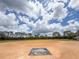 View of the baseball field with well-maintained grass, neatly lined trees, and a bright blue sky filled with fluffy clouds at 9017 Se 119Th St, Summerfield, FL 34491