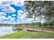 Picturesque lake view with a wooden dock and gazebo, surrounded by lush greenery and blue sky at 9017 Se 119Th St, Summerfield, FL 34491