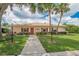 Charming single-story clubhouse with red shutters, mature landscaping, and paved walkway at 451 Village Sw Cir, Winter Haven, FL 33880