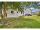 Home exterior featuring white siding, lush lawn, tree, and an outdoor utility access door at 6443 Hollyberry Ne Ln, Winter Haven, FL 33881