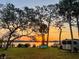 Scenic waterfront property featuring a vibrant sunset, lush green lawn, and mature shade trees at 1949 Bayview Dr, New Smyrna Beach, FL 32168