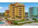 Condo exterior featuring a bright yellow facade, balconies, palm trees, pool, well-manicured lawn, and white picket fence at 701 N Atlantic Ave # 202, New Smyrna Beach, FL 32169