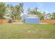 Spacious backyard featuring a wooden fence, lush green grass, mature trees, and a charming blue detached garage at 532 Faulkner St, New Smyrna Beach, FL 32168