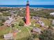 An aerial view of a tall red lighthouse surrounded by smaller houses with a blue ocean horizon at 86 Rains Ct, Ponce Inlet, FL 32127