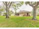 Well-maintained backyard with manicured lawn, patio, mature trees, and beige house exterior at 2626 Turnbull Estates Dr, New Smyrna Beach, FL 32168