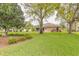 Wide view of backyard, lawn, mature trees, and the exterior of the tan house at 2626 Turnbull Estates Dr, New Smyrna Beach, FL 32168