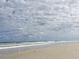 Wide sandy beach with gentle waves under a sky filled with fluffy clouds at 108 Lake Fairgreen Cir, New Smyrna Beach, FL 32168